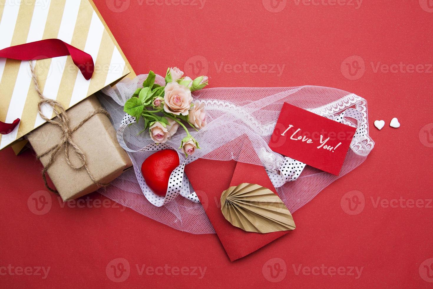 From a gift bag flat lay a gift, an envelope, a heart, flowers and tulle with I love you text on card. Valentine's Day concept photo