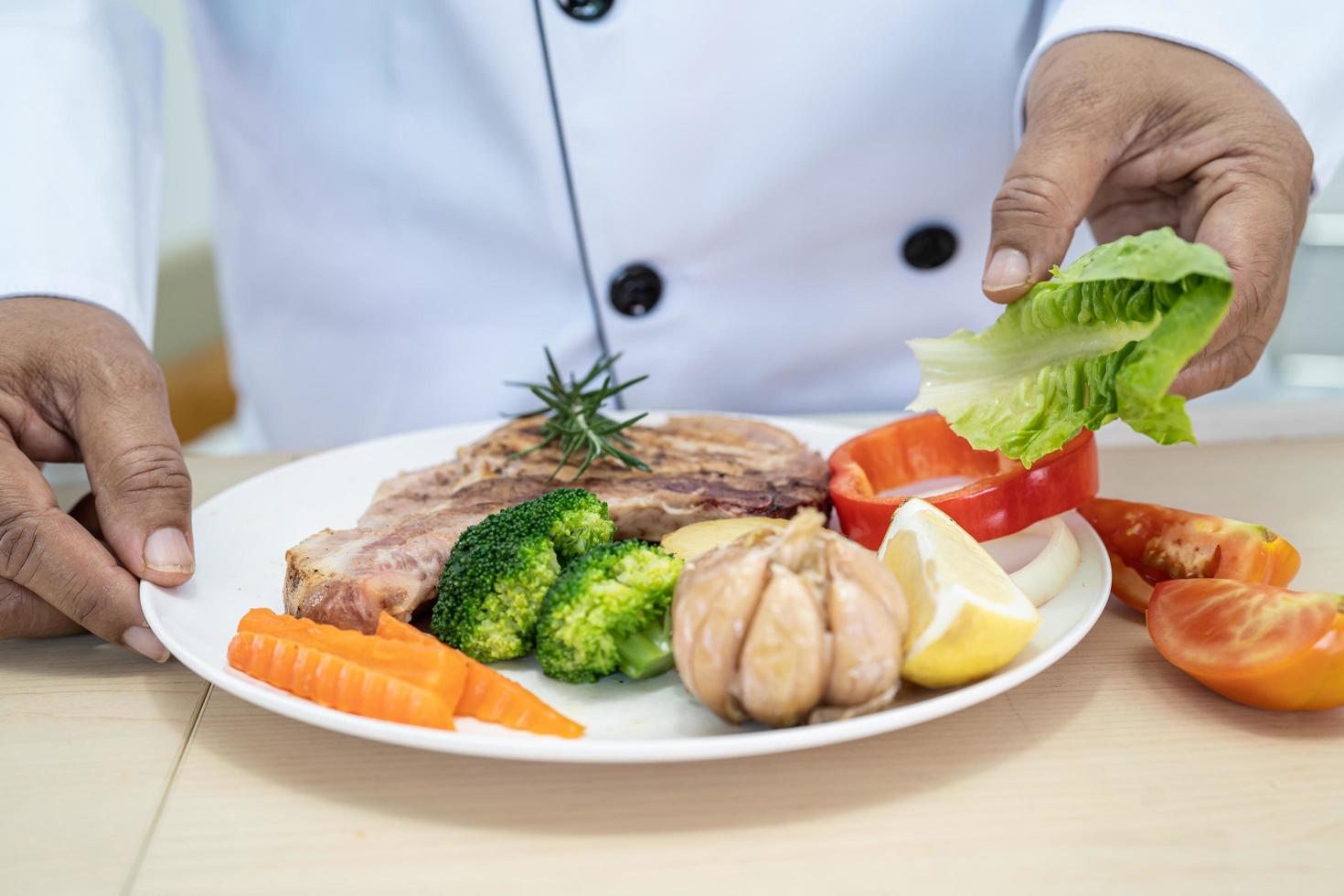 el chef prepara y cocina un plato de bistec de cerdo y ensalada trabajando en la cocina de un hotel o restaurante. foto