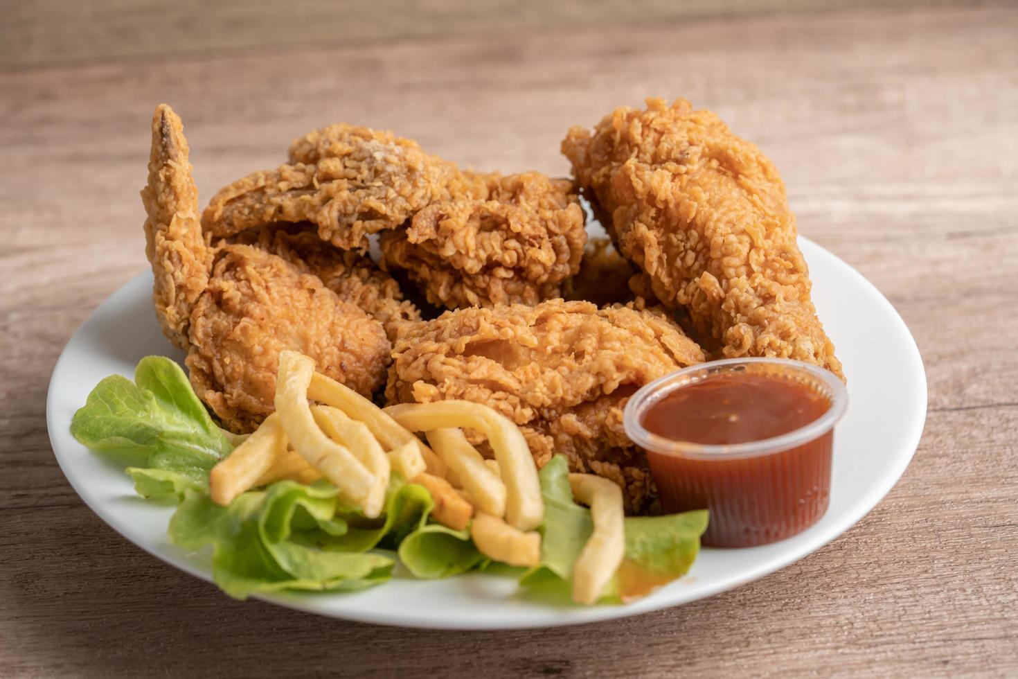 Pollo frito y papas fritas con hojas de romero, comida chatarra alta en calorías servida en un plato blanco foto