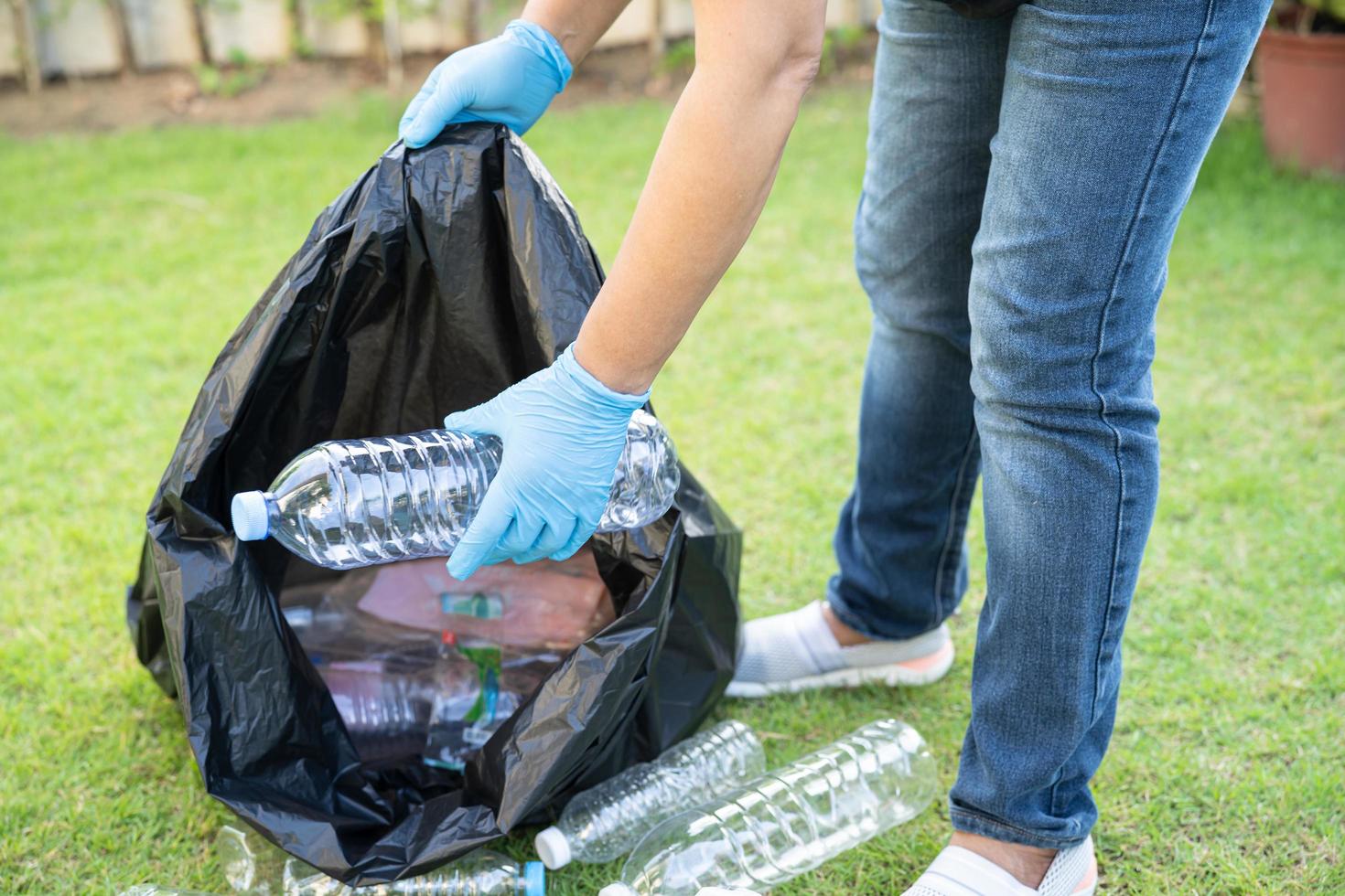 Voluntario de mujer asiática lleva botellas de plástico de agua a la basura de la bolsa de basura en el parque, recicla el concepto de ecología ambiental de residuos. foto