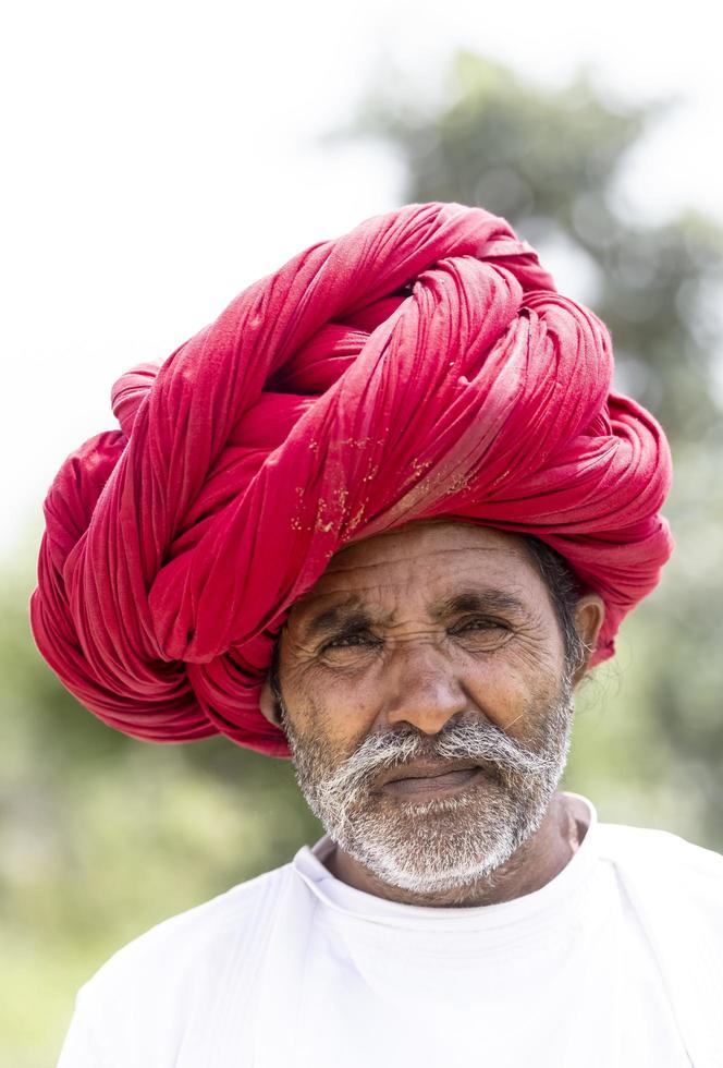 Portrait of an elderly man of the Rabari ethnic group in a national headdress and traditional white dress on the field on bera. photo