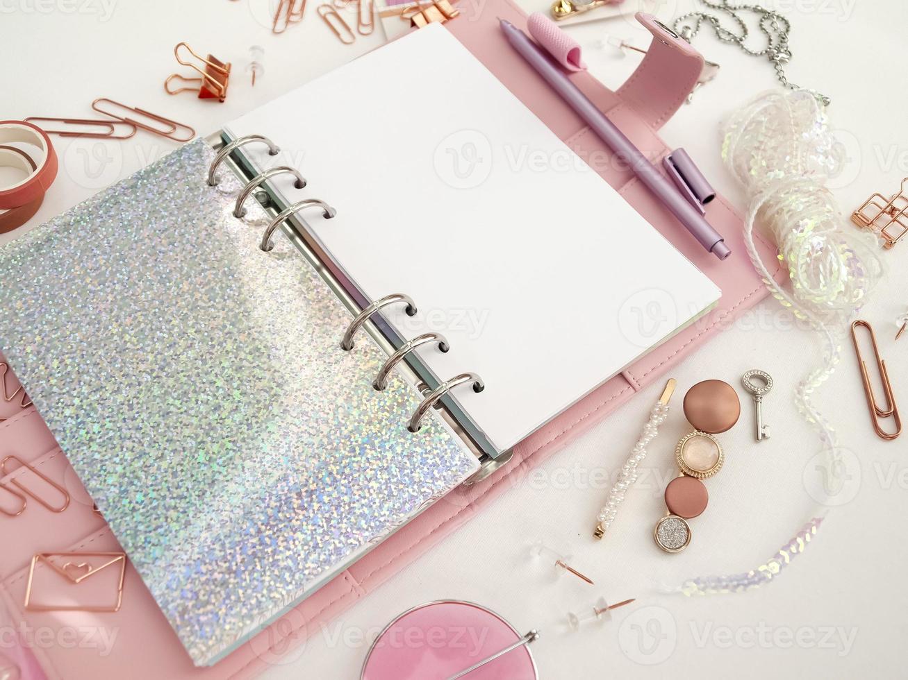 Diary opens with white and holographic page. Pink planner with cute stationery photographing in flatlay style. Top view of pink planner with business stationery. Pink glamour planner decoration photo