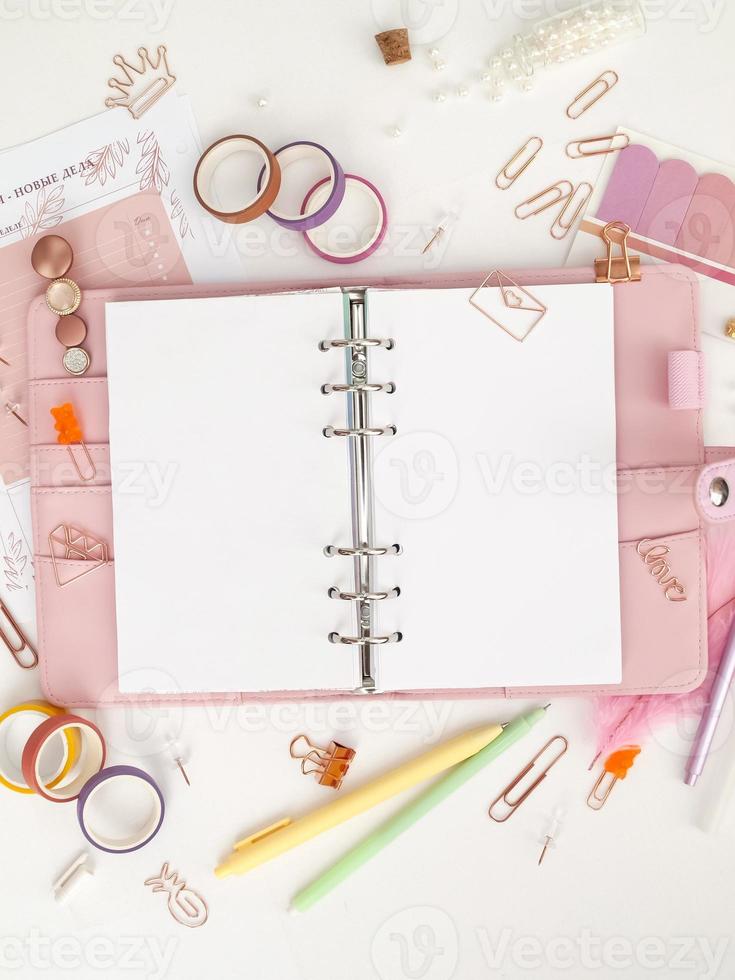 Diary opens with white and holographic page. Pink planner with cute stationery photographing in flatlay style. Top view of pink planner with business stationery photo