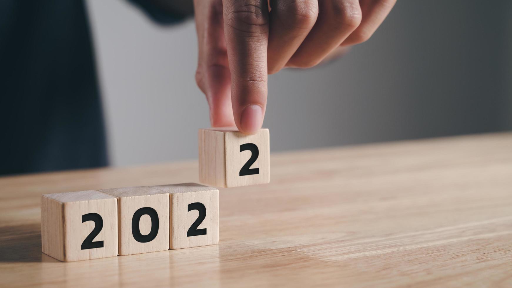 Mano de hombre poniendo un bloque de cubo de madera para cambiar el año 2021 al año 2022 en la mesa de madera con espacio de copia. comienzo del año 2022. feliz año nuevo concepto. foto