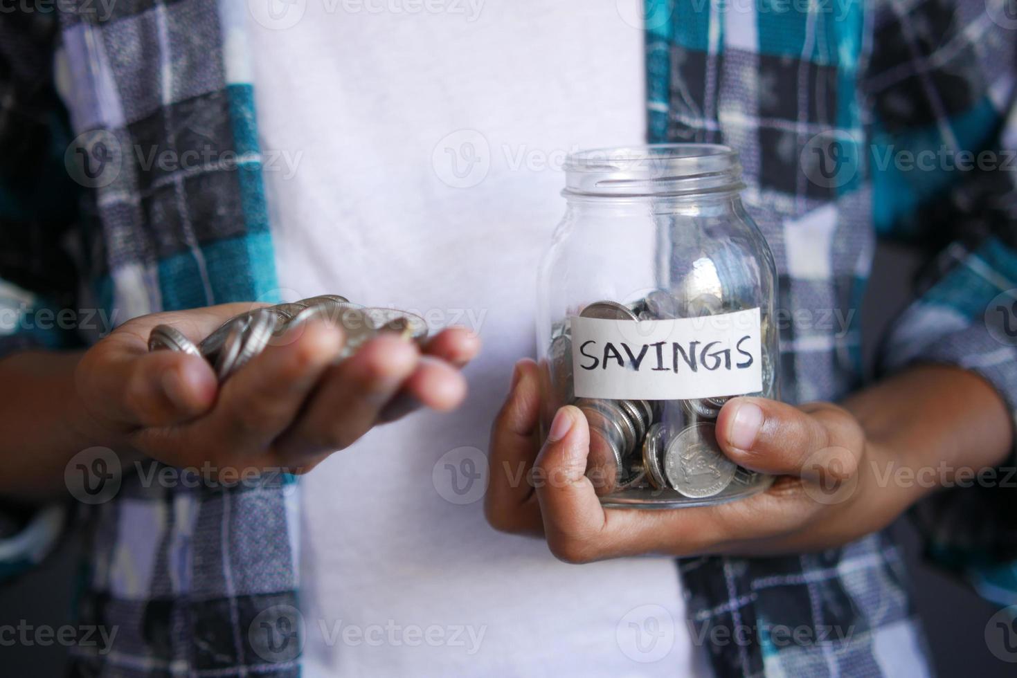 Joven ahorrando monedas en un frasco situado en blanco foto