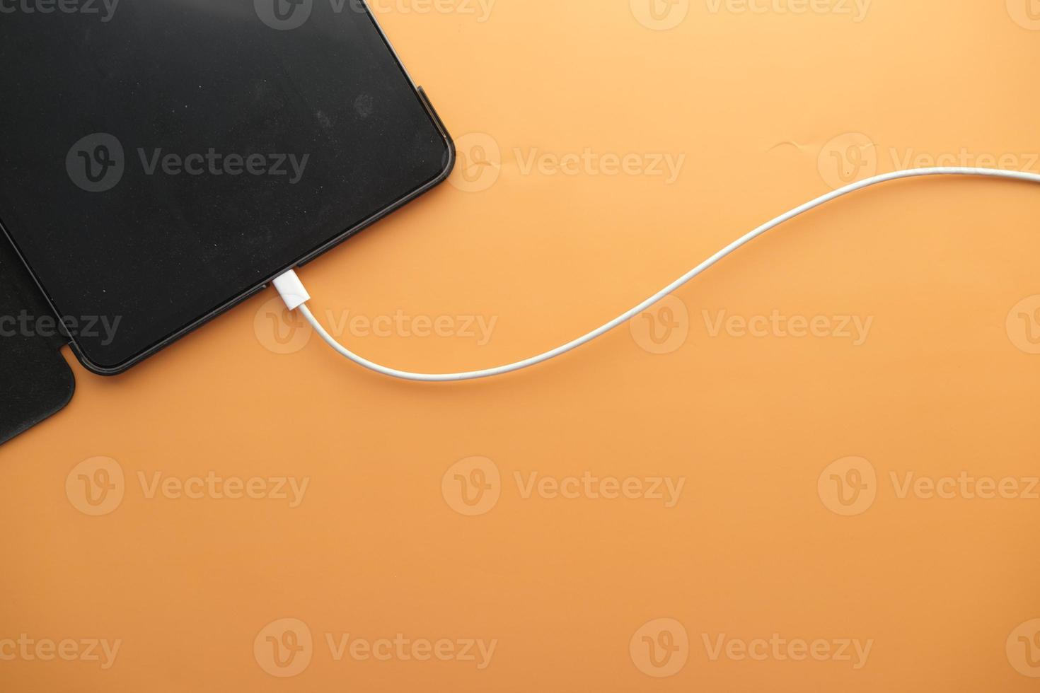 charging smart phone with a cable on color background photo