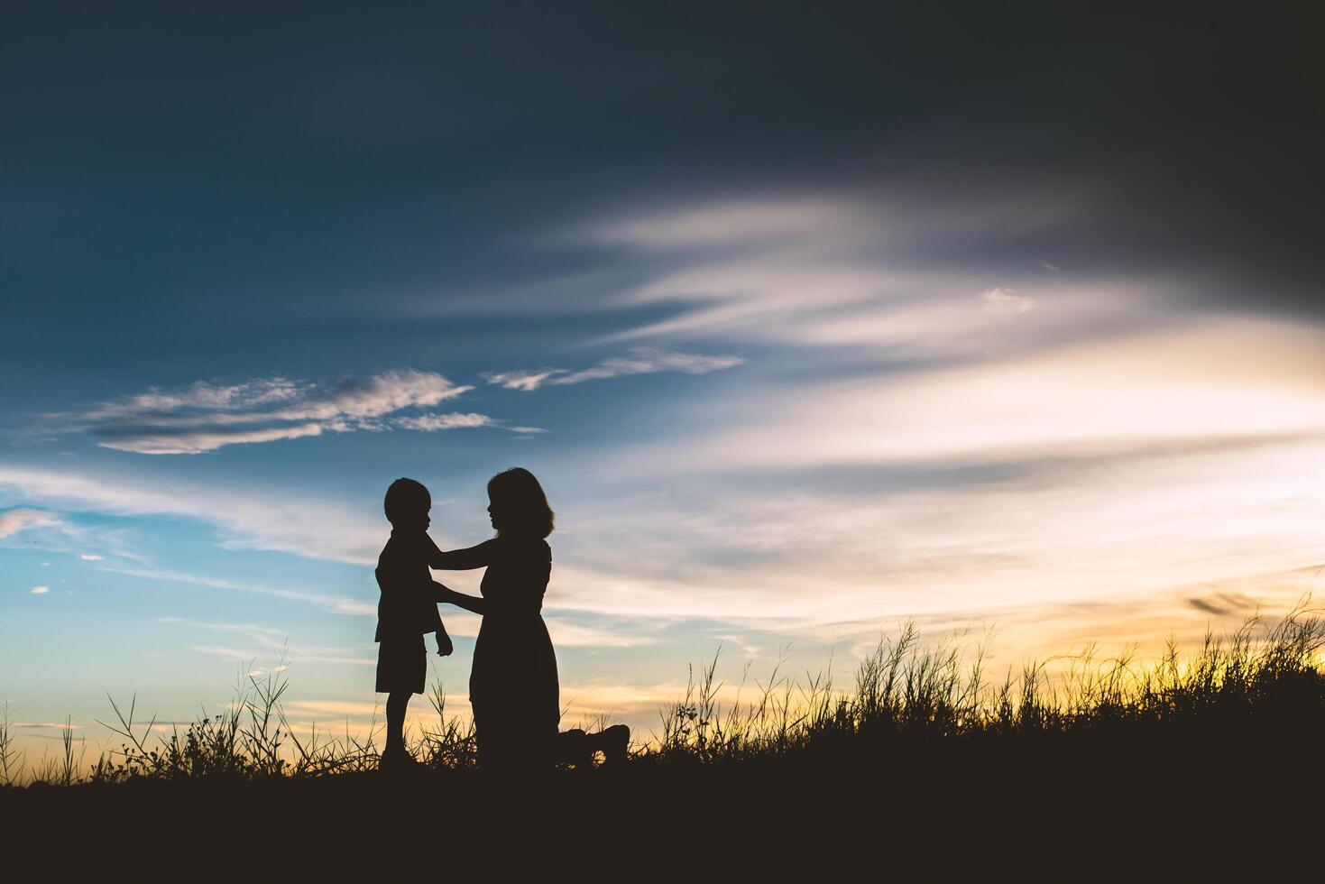 Mother encouraged her son outdoors at sunset, silhouette concept photo