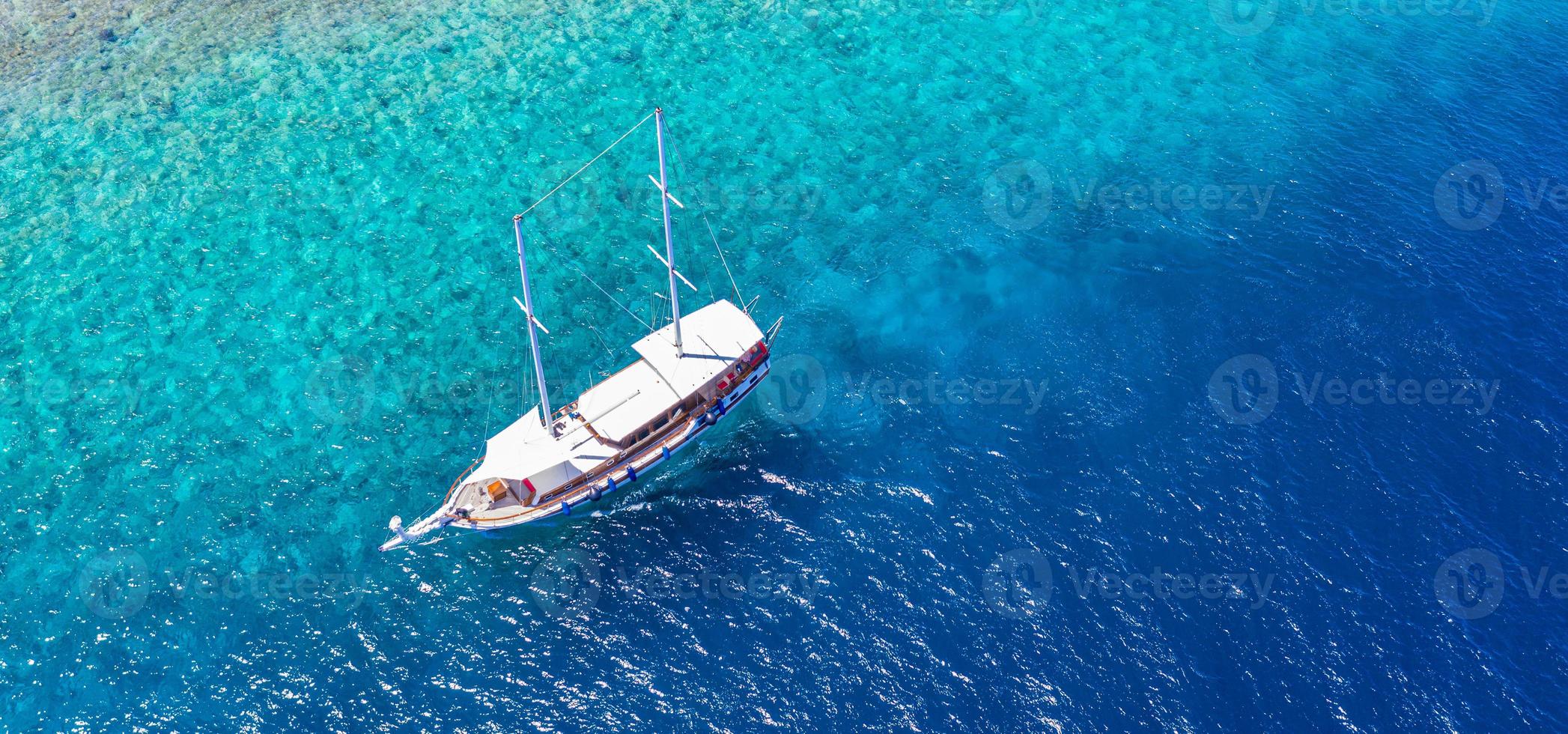 Yacht anchoring in crystal clear turquoise water in front of the tropical island, recreational lifestyle, snorkeling. Aerial view of yacht at anchor on turquoise water, luxury activity, Maldives tour photo