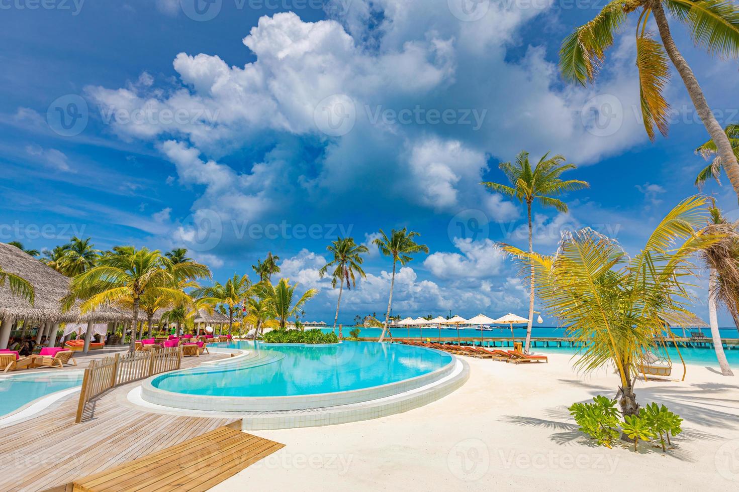 Outdoor tourism landscape. Luxurious beach resort with swimming pool and beach chairs or loungers under umbrellas with palm trees and blue sky. Summer travel and vacation background concept photo