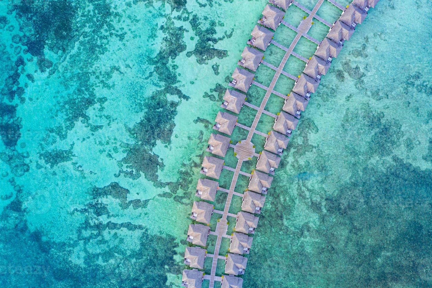 villas de lujo sobre el agua desde arriba. vista aérea de drones. villas de agua con increíble playa de mar y laguna, naturaleza tropical. banner de destino de turismo exótico, vacaciones de verano foto