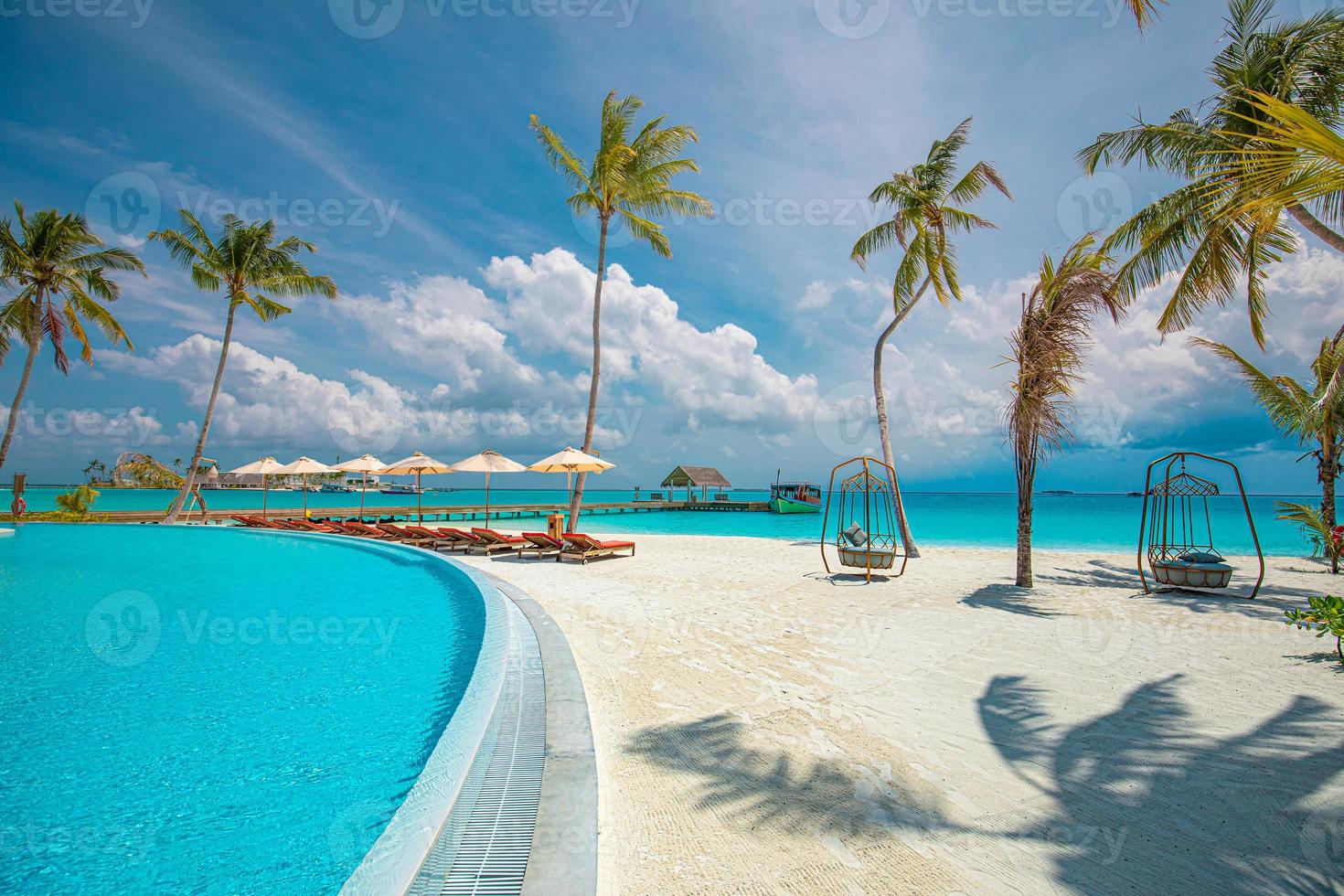 paisaje de turismo al aire libre. lujoso resort de playa con piscina y sillas de playa o tumbonas bajo sombrillas con palmeras y cielo azul. concepto de fondo de viajes y vacaciones de verano foto