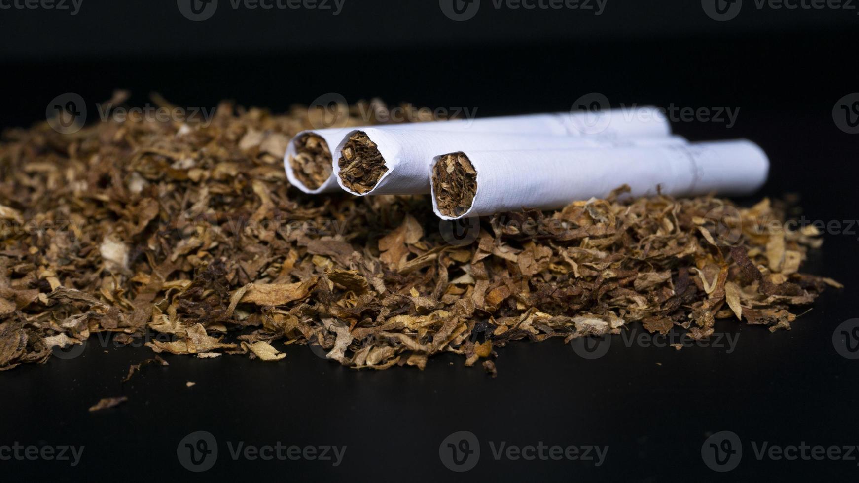 montón de tabaco y algunos cigarrillos sobre un fondo negro foto