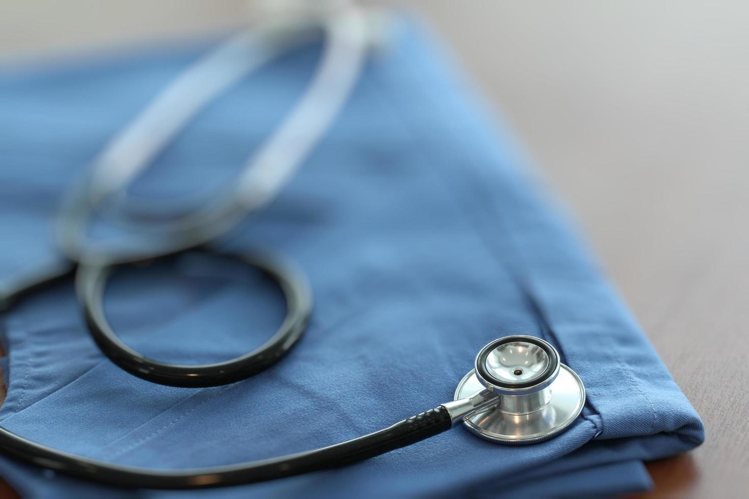 Stethoscope with blue doctor coat on wooden table with shallow DOF evenly matched and background photo