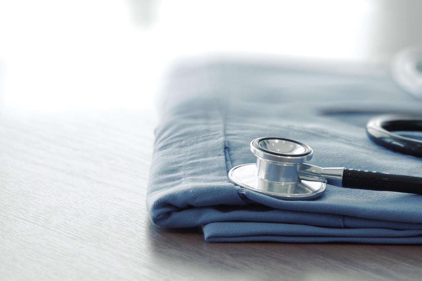 Stethoscope with blue doctor coat on wooden table with shallow DOF evenly matched and background photo