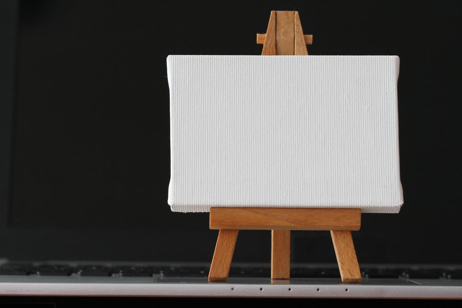 blank canvas and wooden easel on laptop computer as concept photo