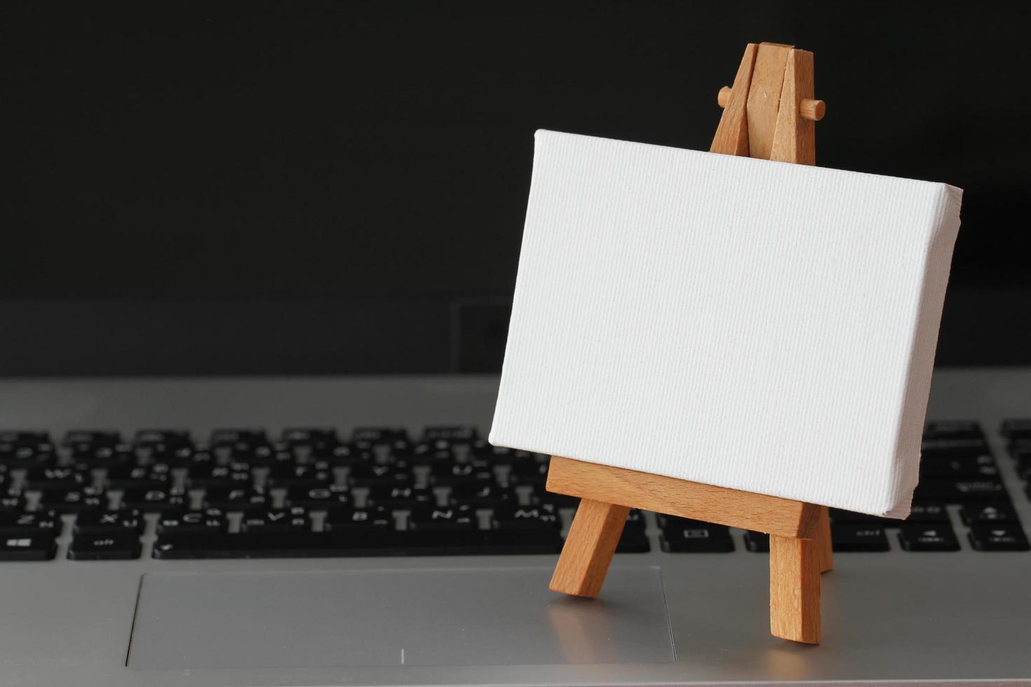 blank canvas and wooden easel on laptop computer as concept photo