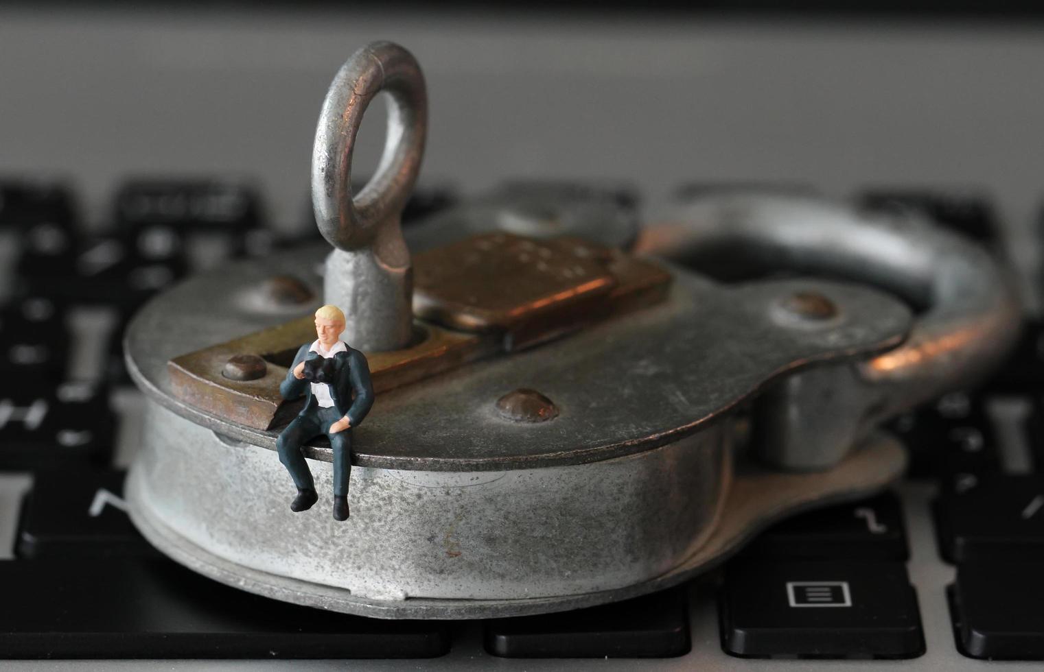 Internet security concept-miniature businessman stand on old key and padlock on laptop computer keyboard photo