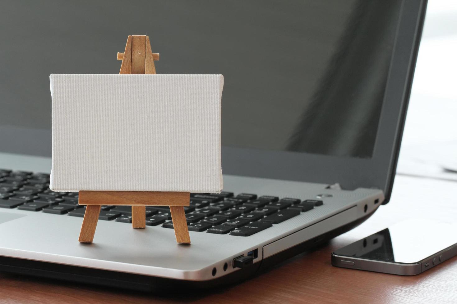 Lienzo en blanco y caballete de madera en la computadora portátil como concepto foto