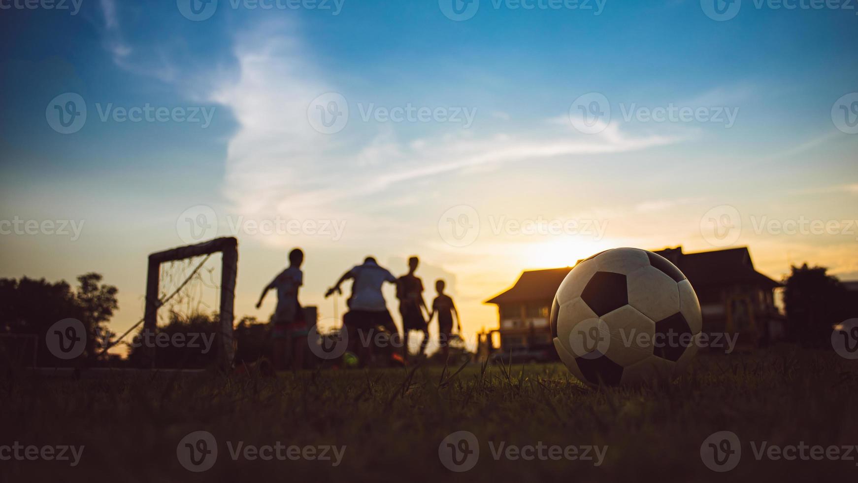 Silhouette action sport outdoors of kids having fun playing soccer football for exercise in community rural area under the twilight sunset sky photo