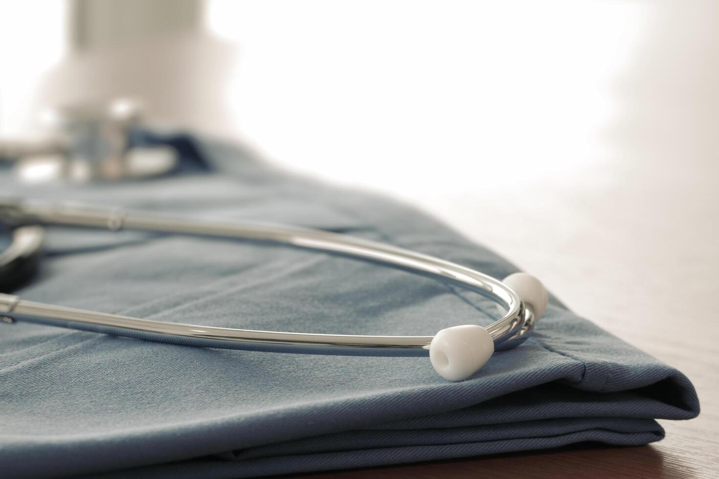 Stethoscope with blue doctor coat on wooden table with shallow DOF evenly matched and background photo