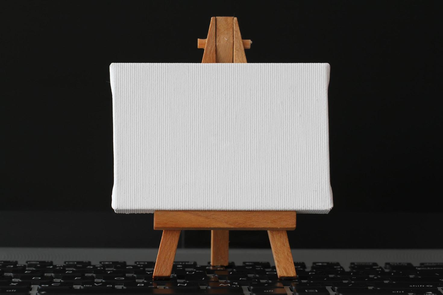 blank canvas and wooden easel on laptop computer as concept photo