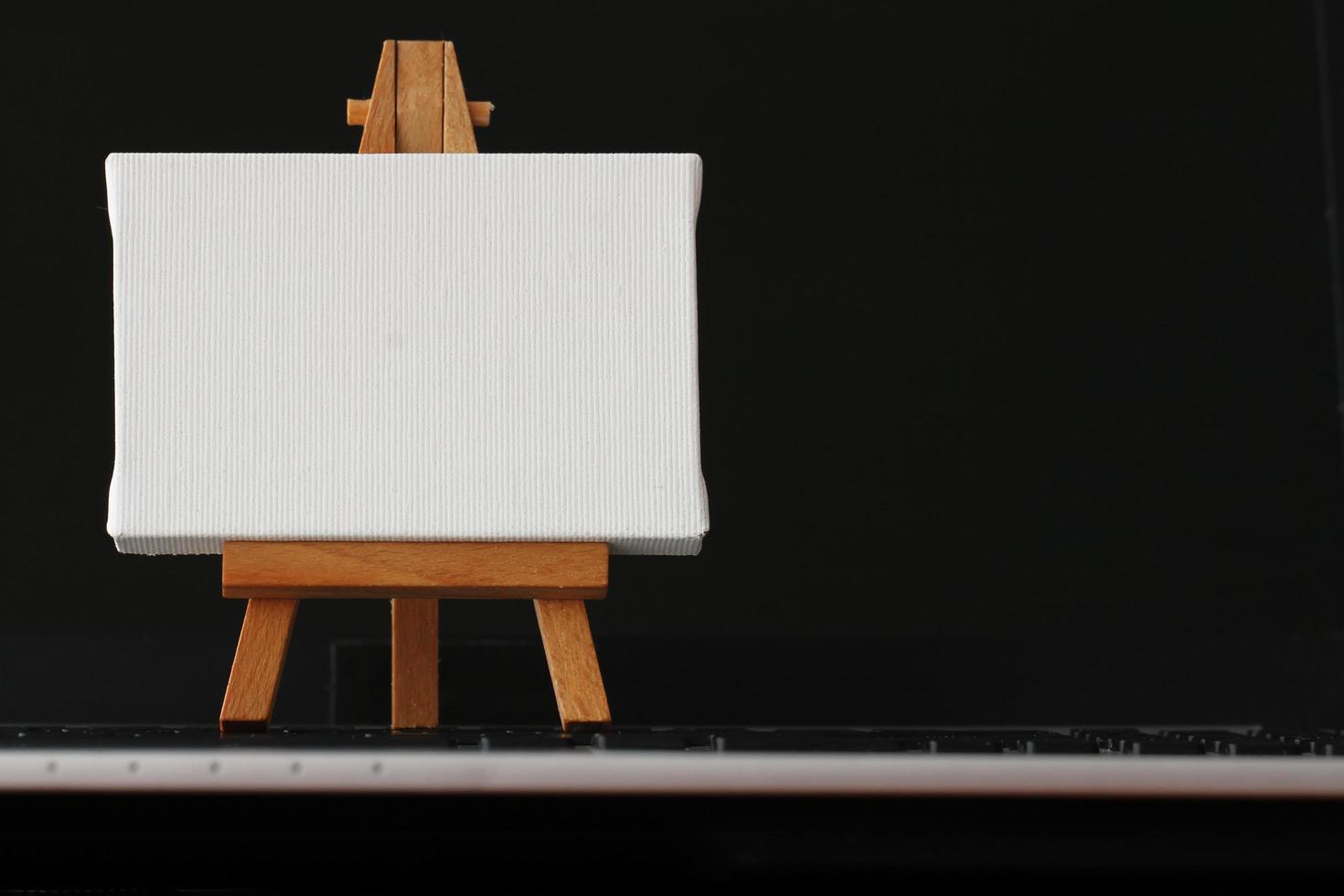 blank canvas and wooden easel on laptop computer as concept photo