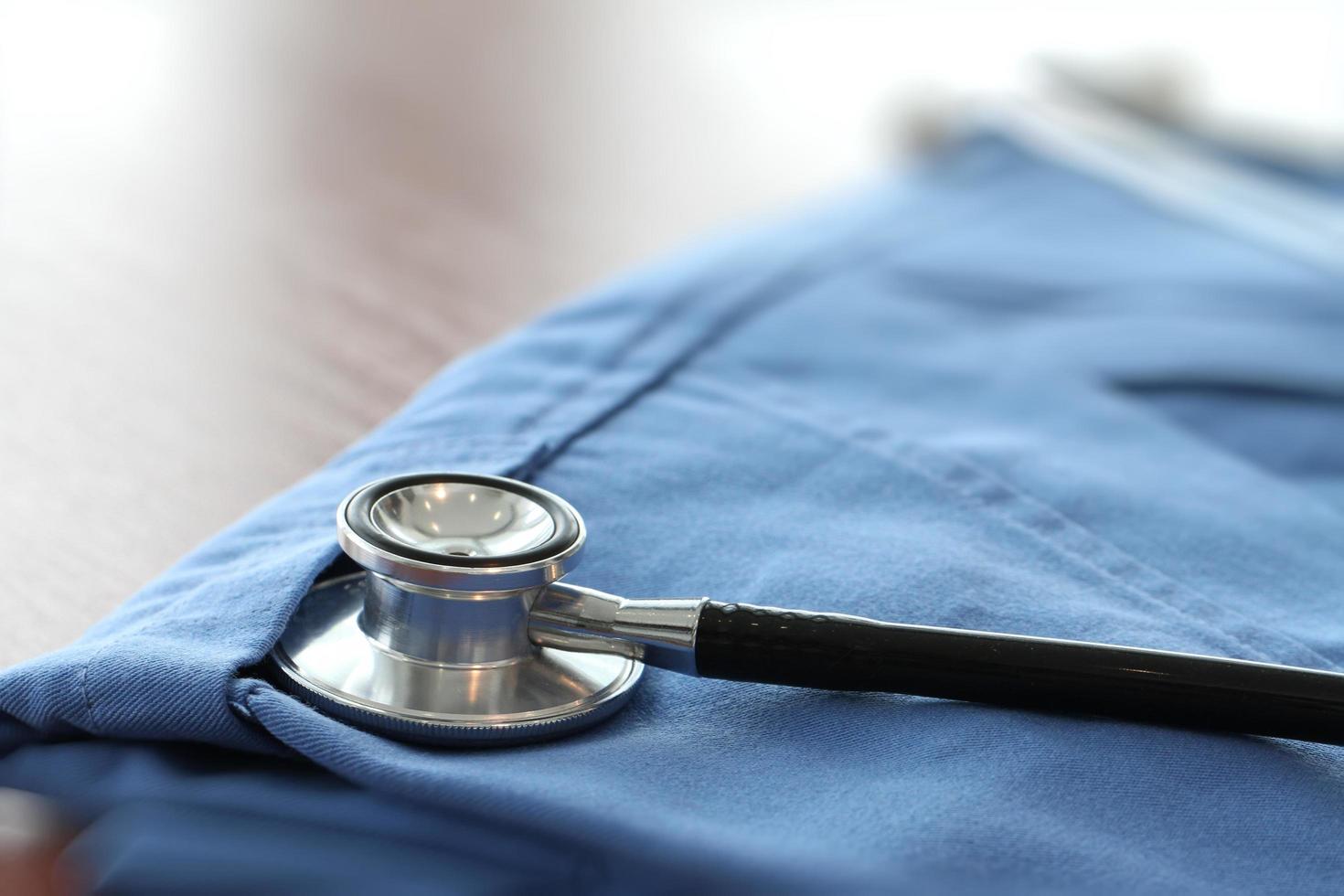 Stethoscope with blue doctor coat on wooden table with shallow DOF evenly matched and background photo