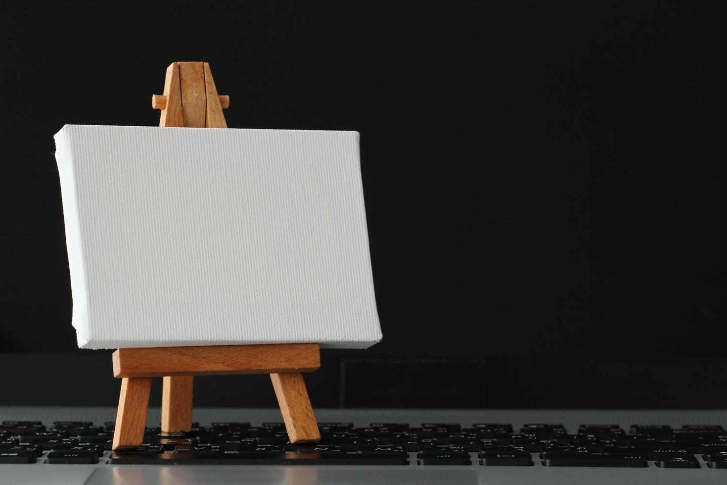 blank canvas and wooden easel on laptop computer as concept photo