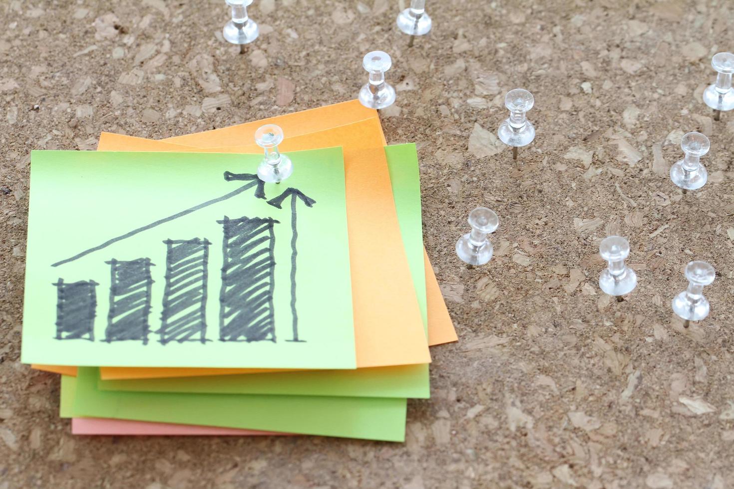 close up of pin and hand drawn business strategy graph chart on sticky note with cork board as concept photo