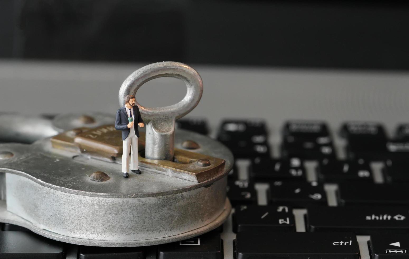 Concepto de seguridad en Internet: empresario en miniatura se para en una llave antigua y candado en el teclado de la computadora portátil foto