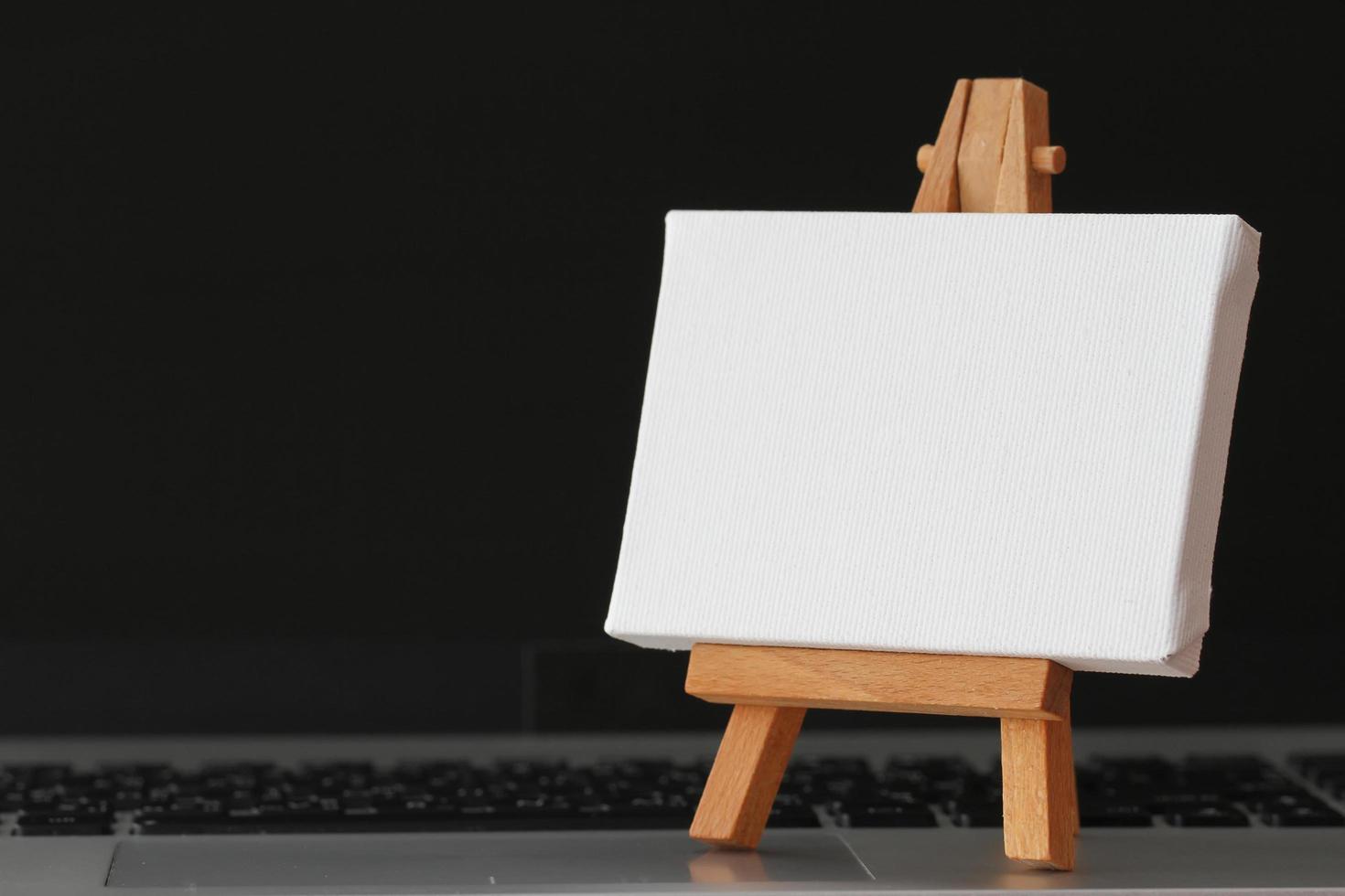 blank canvas and wooden easel on laptop computer as concept photo