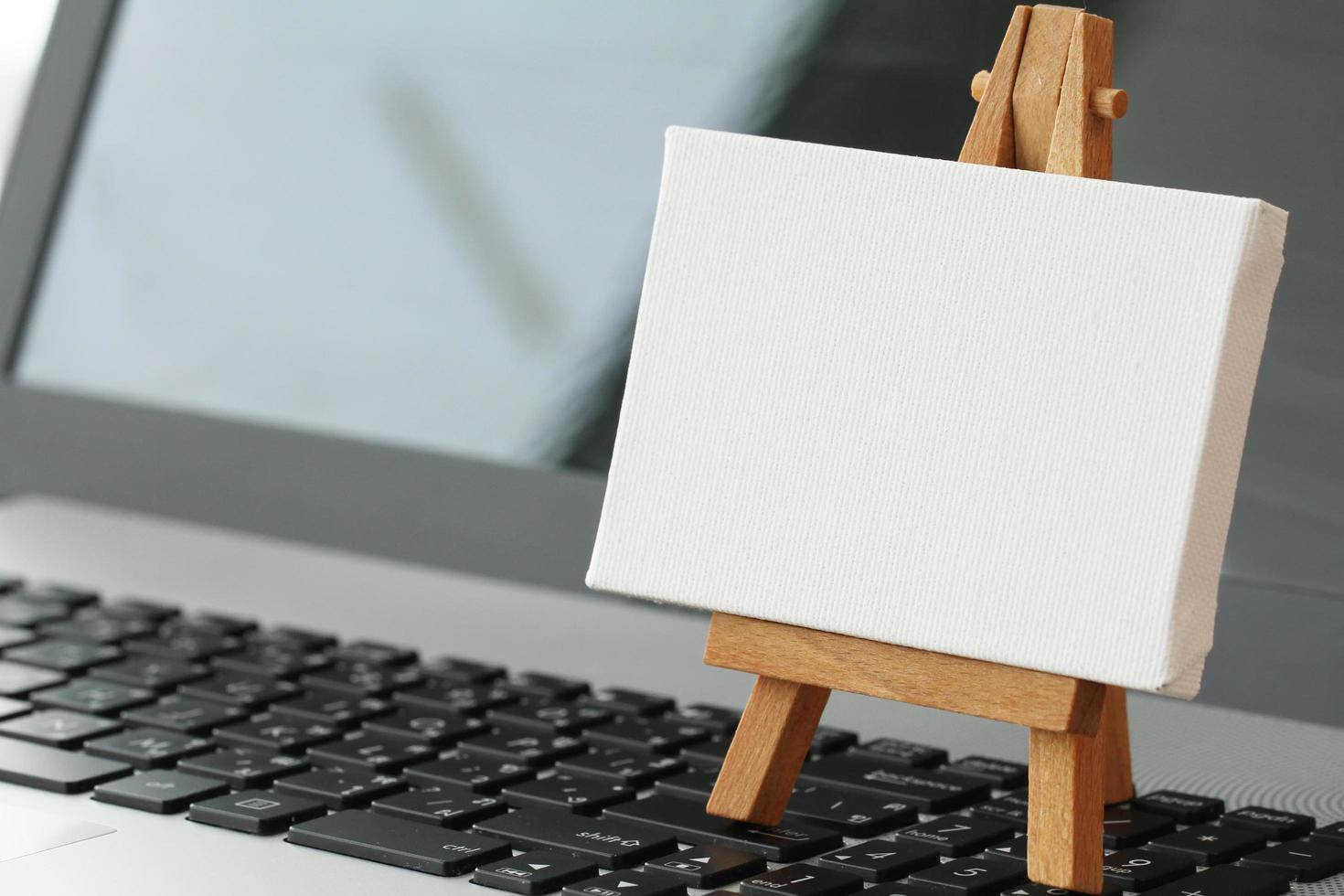 blank canvas and wooden easel on laptop computer as concept photo