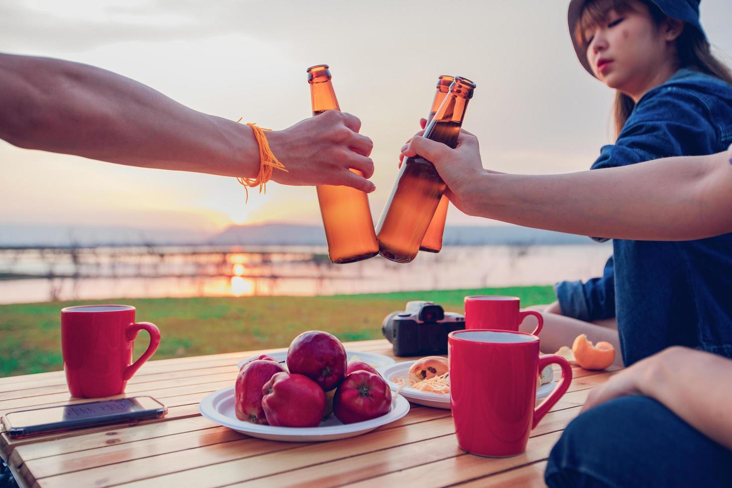 A group of Asian friends tourist drinking alcoholic beer and playing guitar together with happiness in Summer while having camping near lake at sunset photo