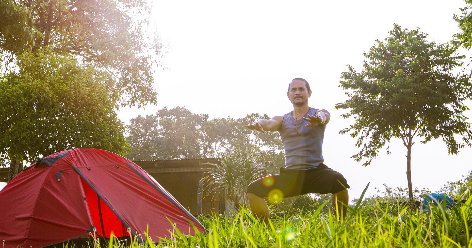 un hombre hace ejercicio y un atleta se calienta por la mañana cerca de una tienda de campaña en un viaje de campamento en la montaña foto