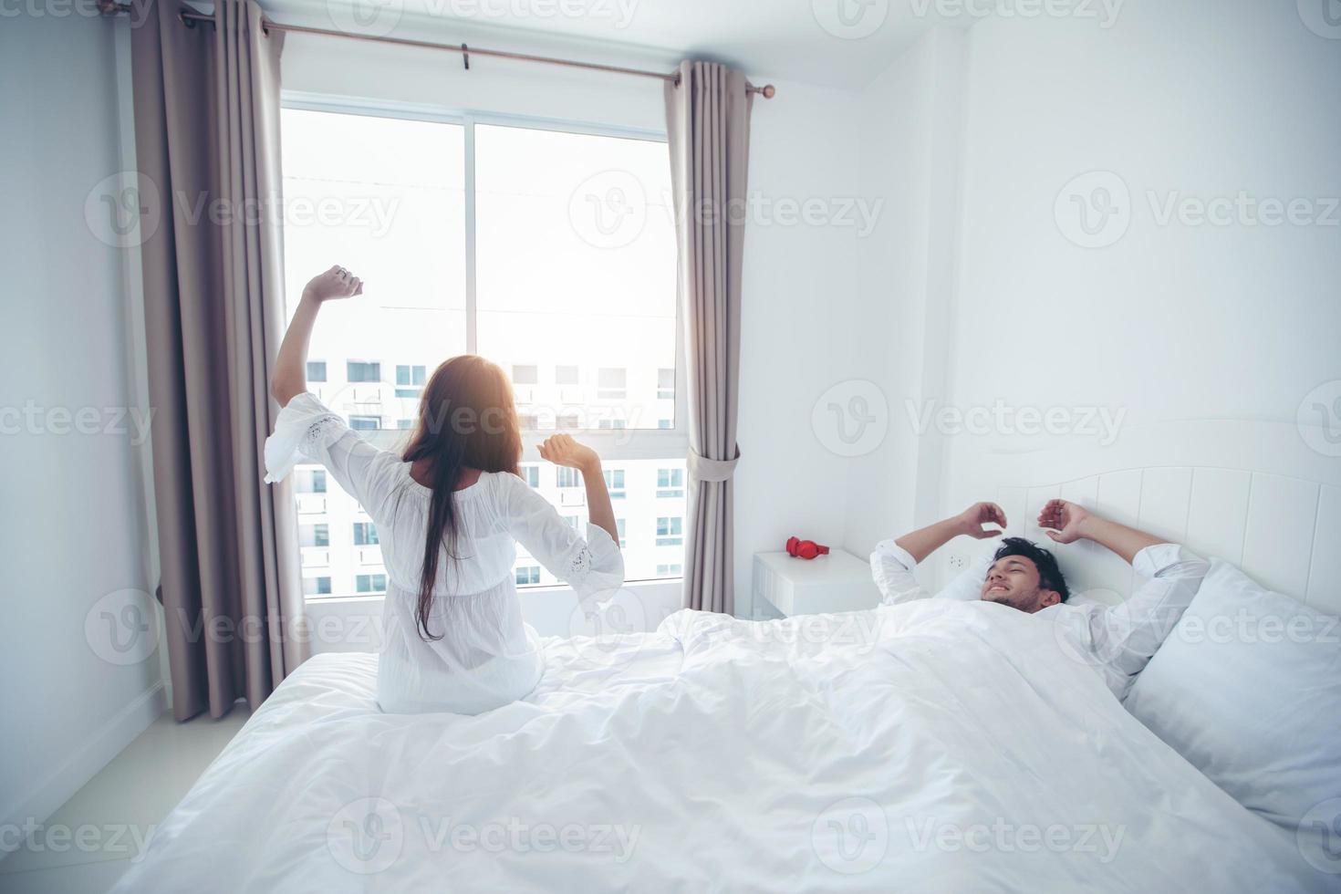 Amante de las parejas que se despierta en su cama completamente descansada y abre las cortinas por la mañana para que entre aire fresco. foto