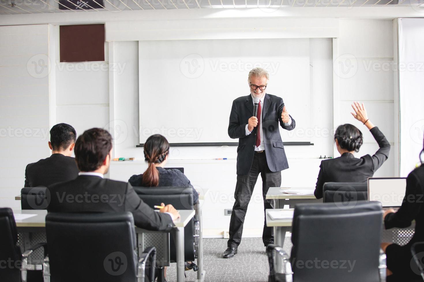 audiencia de negocios levantando la mano mientras el empresario está hablando en formación para la opinión con el líder de la reunión en la sala de conferencias foto