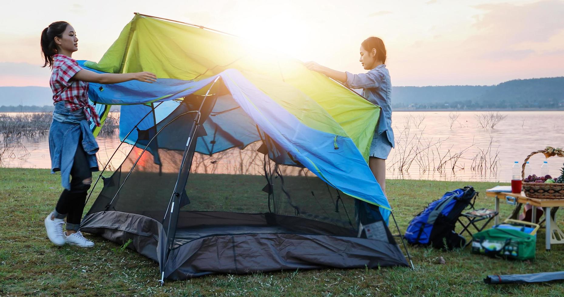 A group of Asian friends tourist drinking and playing guitar together with happiness in Summer while having camping near lake at sunset photo