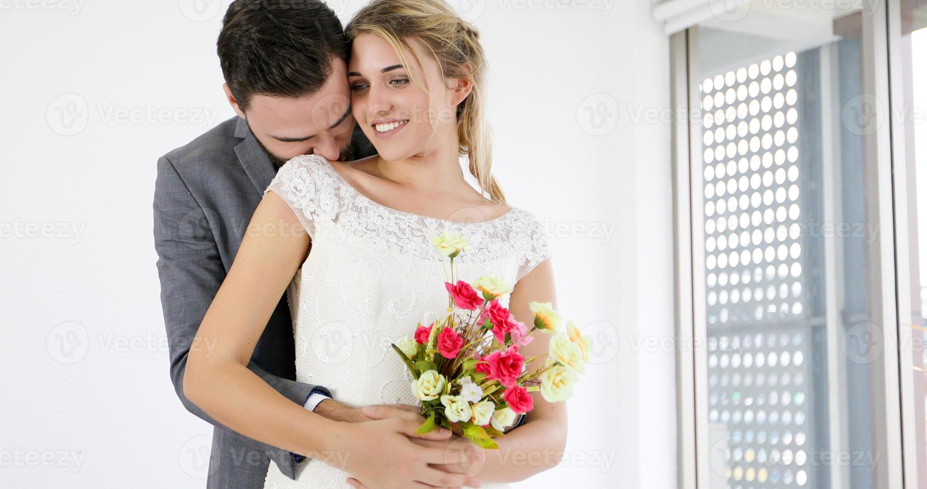 los amantes le dan flores a la novia y se besan felices y la pareja ama de pie en el estudio de bodas foto