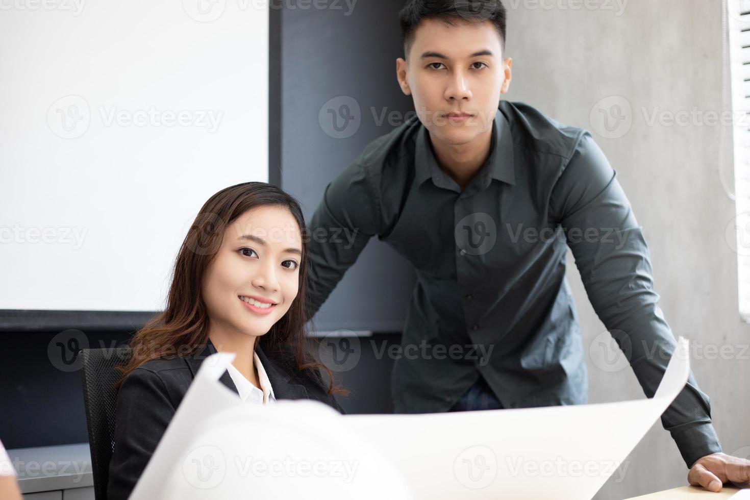 Grupo de hombres de negocios e ingenieros que usan un cuaderno para socios comerciales que discuten documentos e ideas en una reunión y mujeres de negocios que sonríen felices por trabajar foto