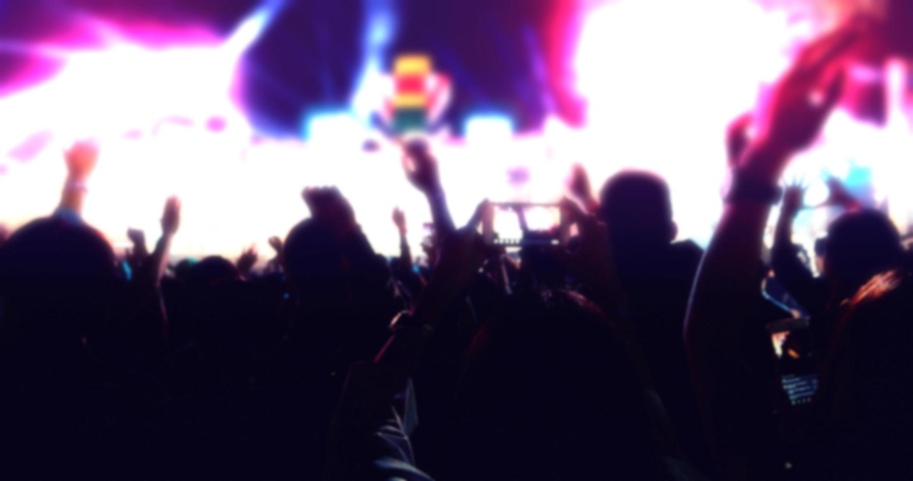 blurry of silhouettes of concert crowd at Rear view of festival crowd raising their hands on bright stage lights photo