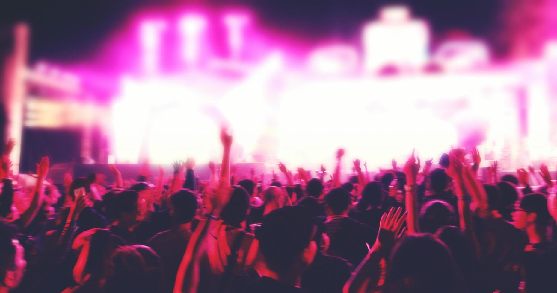 blurry of silhouettes of concert crowd at Rear view of festival crowd raising their hands on bright stage lights photo