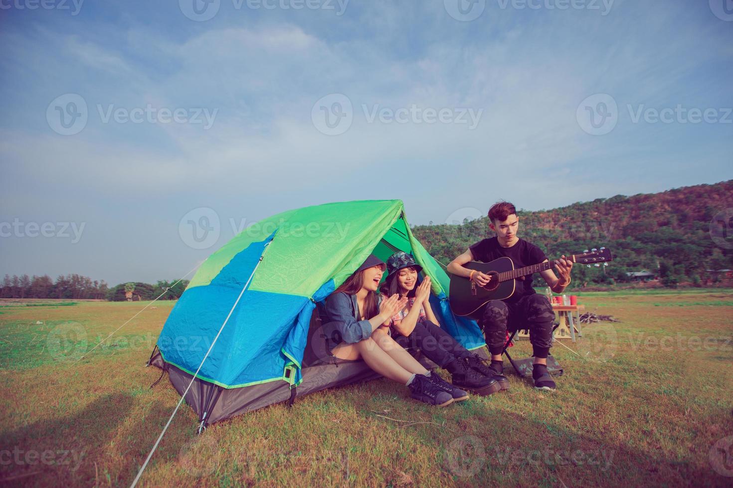 un grupo de amigos asiáticos turistas bebiendo y tocando la guitarra juntos con felicidad en verano mientras acampan cerca del lago al atardecer foto
