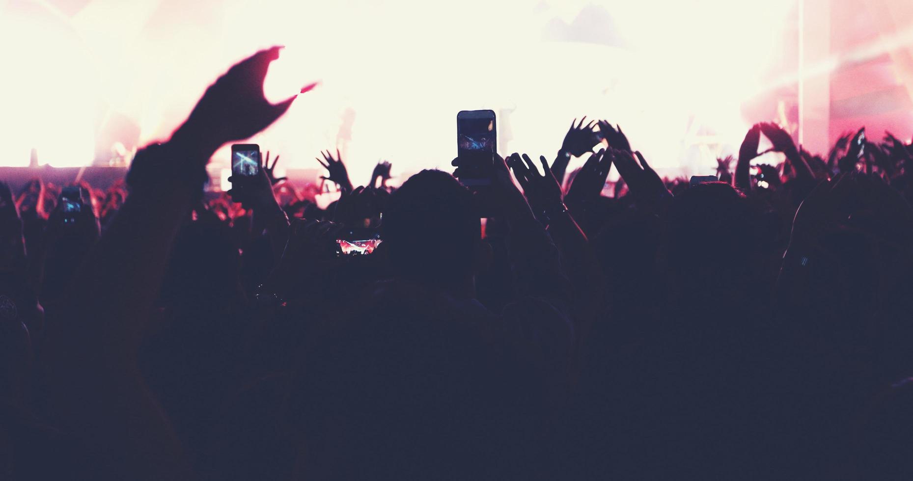 blurry of silhouettes of concert crowd at Rear view of festival crowd raising their hands on bright stage lights photo