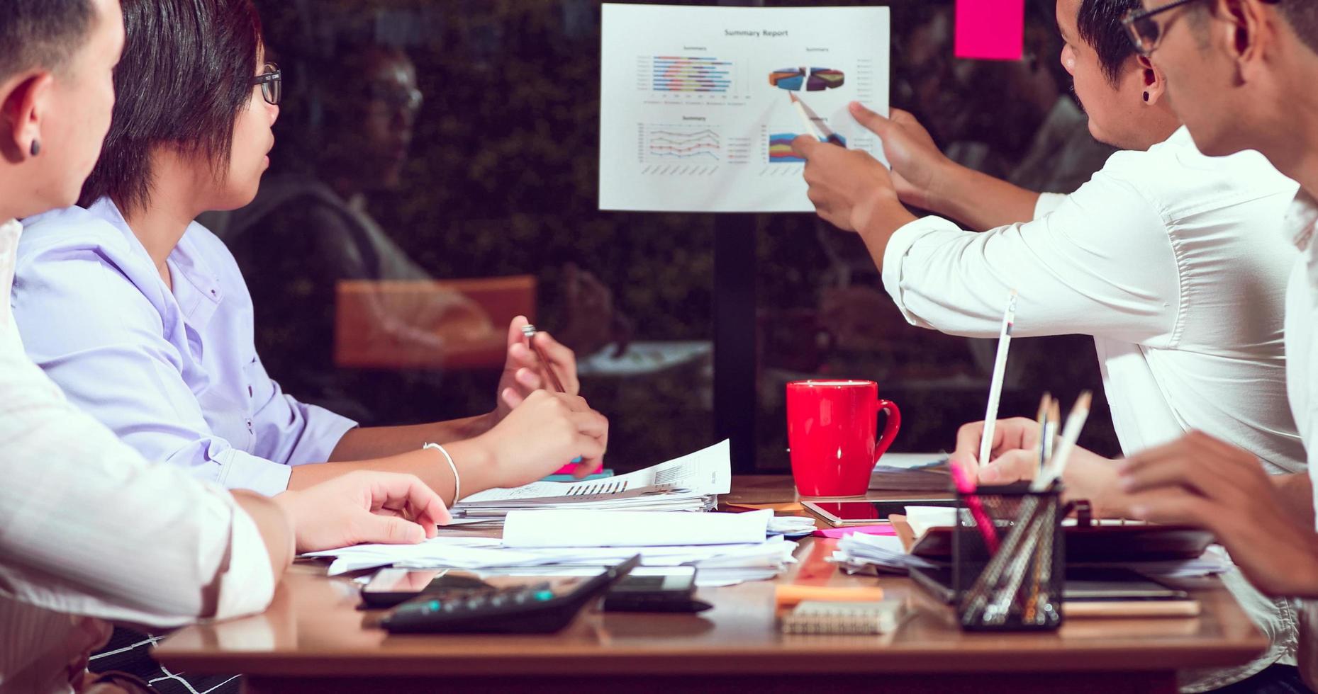 Asian businessmen and businesswomen analysis documents on office table with laptop computer and graph financial diagram working in the background photo