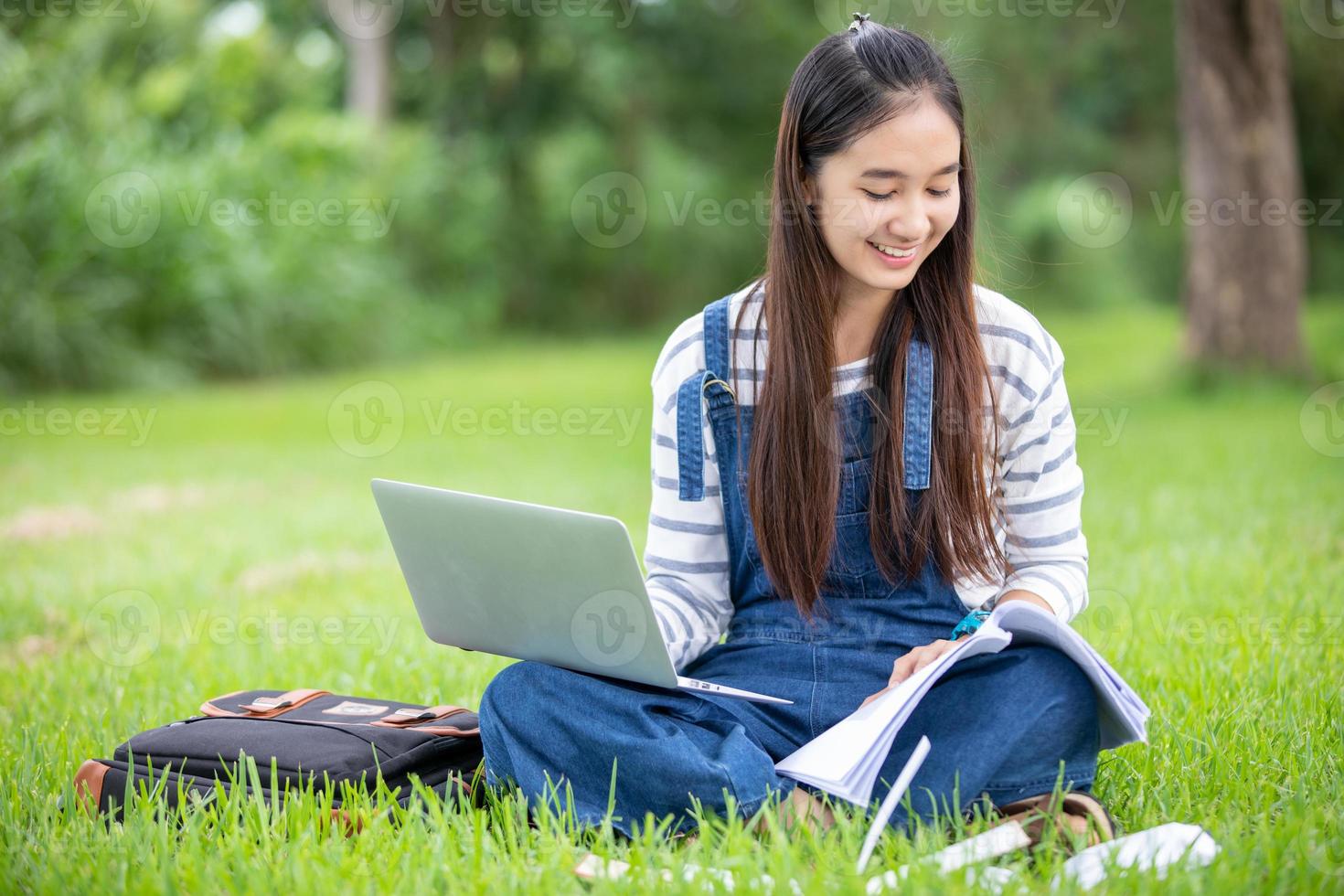 hermosa estudiante asiática sosteniendo libros y sonriendo a la cámara y el concepto de aprendizaje y educación en el parque en verano para relajarse foto