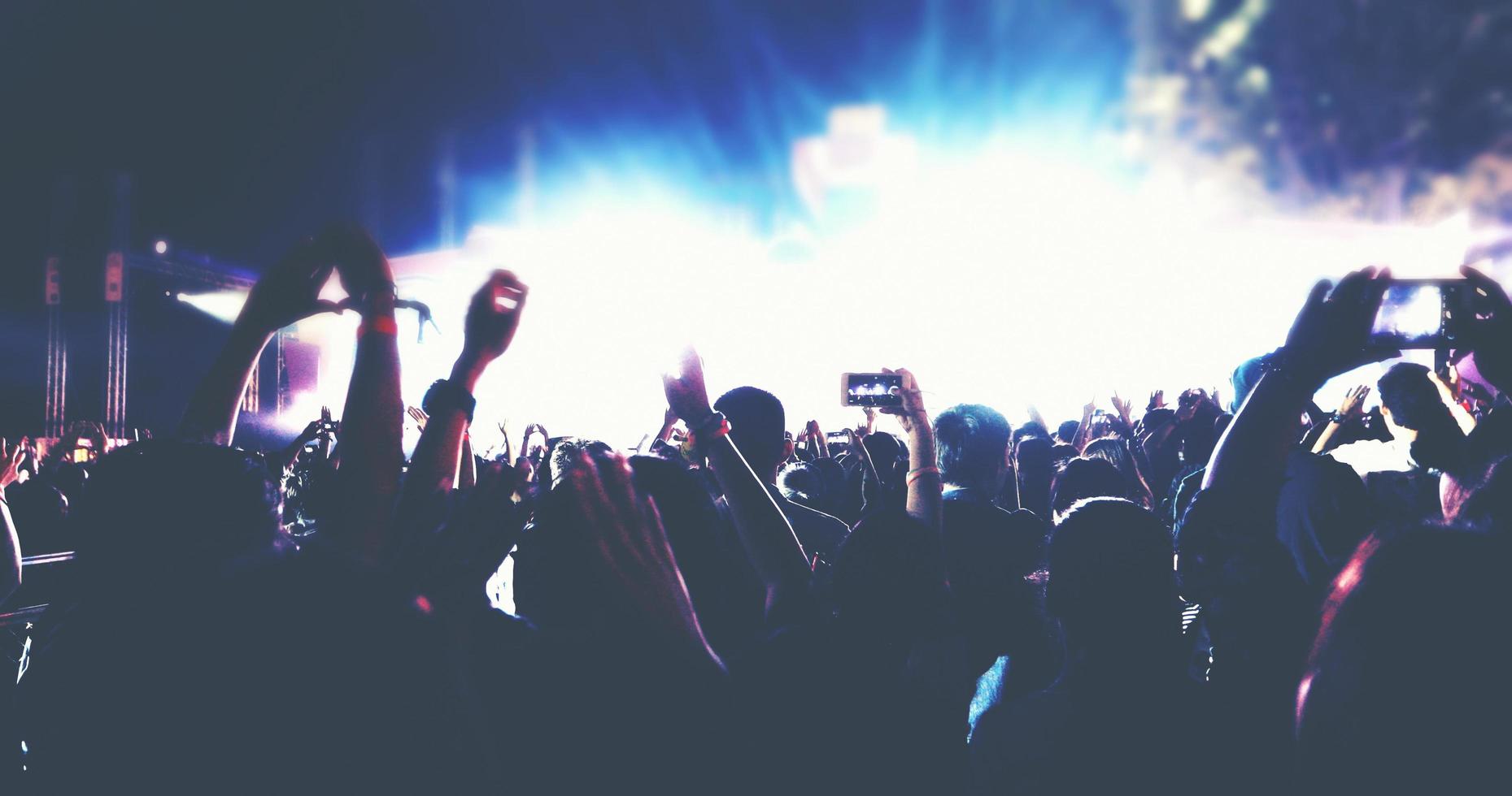 siluetas borrosas de la multitud de conciertos en la vista trasera de la multitud del festival levantando las manos en las luces brillantes del escenario foto