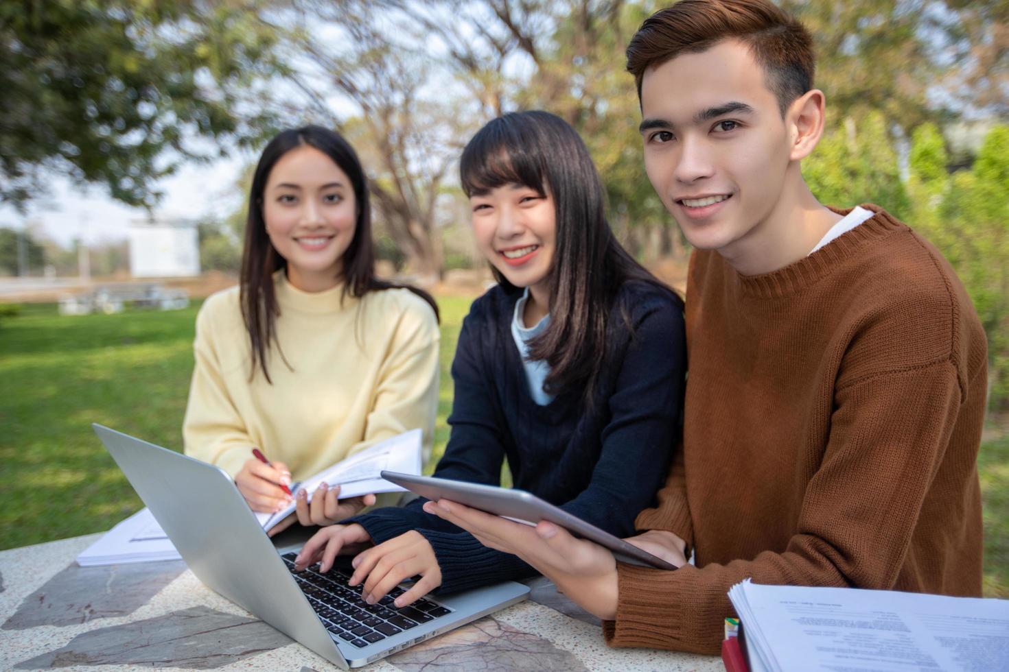 Grupo de estudiantes universitarios asiáticos sentados en la hierba verde trabajando y leyendo juntos al aire libre en un parque foto