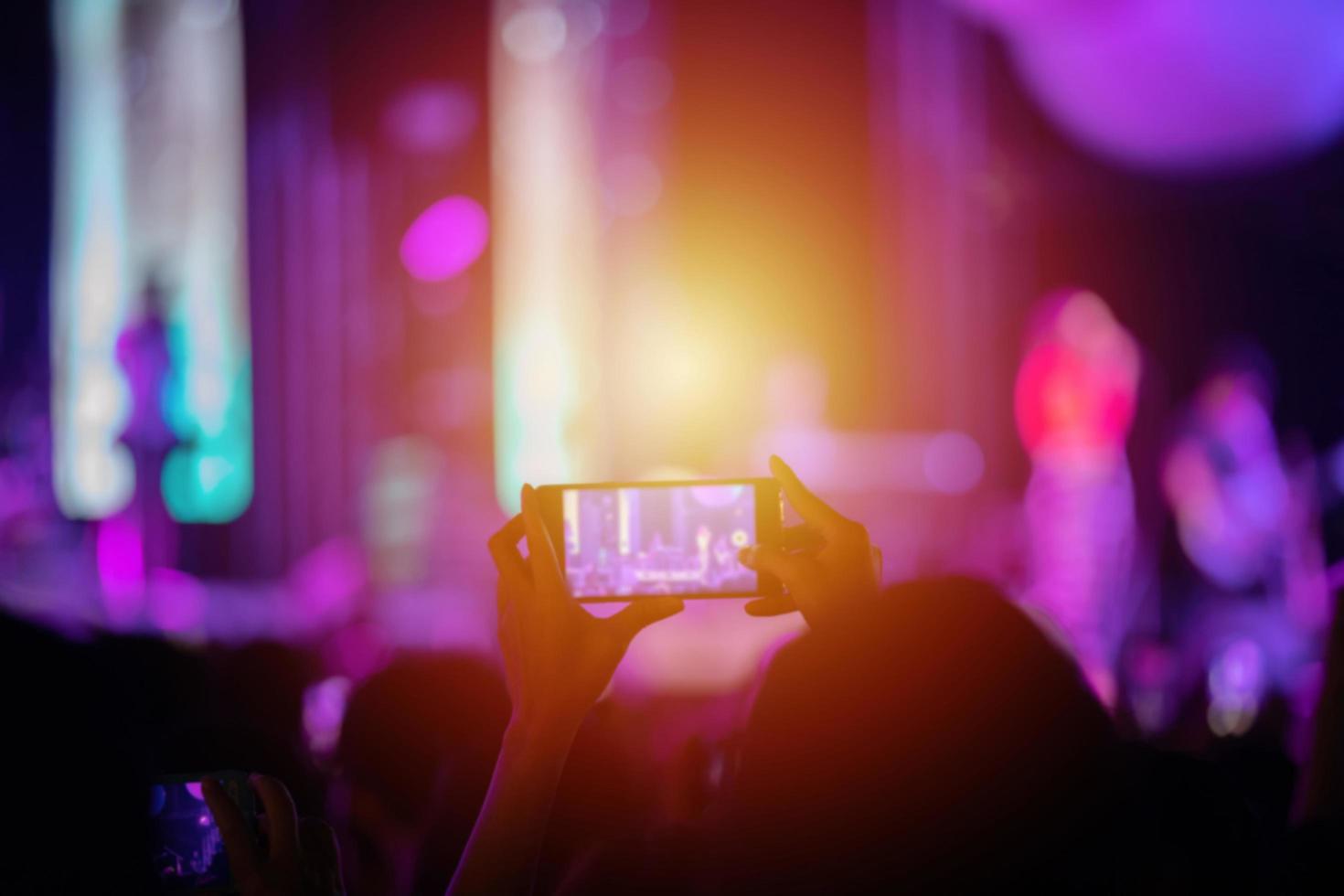 silhouettes of concert crowd at Rear view of festival crowd raising their hands and using smartphone take photo and video on bright stage lights