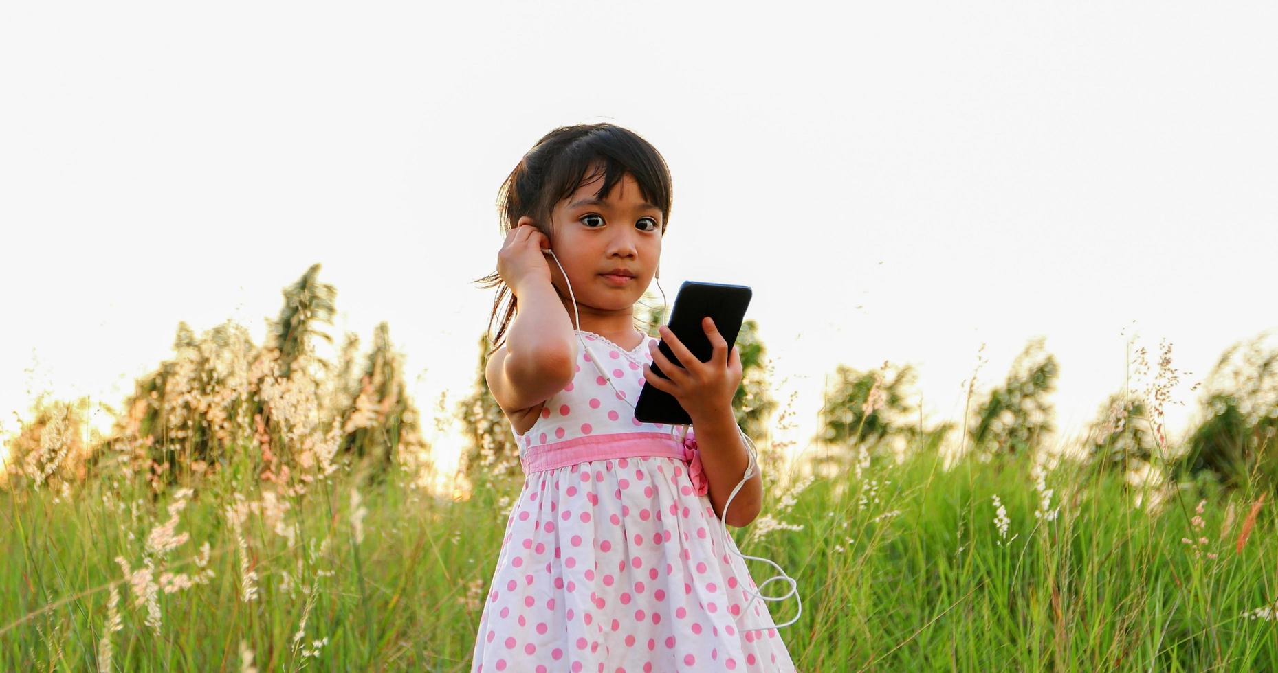 niña asiática escuchando música y cantando desde un teléfono móvil y feliz en la pradera en verano en la naturaleza foto