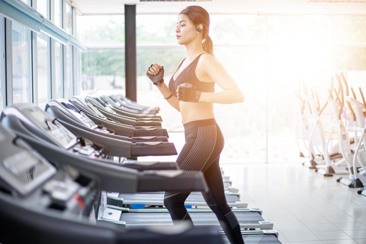 Las mujeres asiáticas corriendo zapatos deportivos en el gimnasio, mientras que una joven mujer caucásica está haciendo jogging en la cinta de correr foto